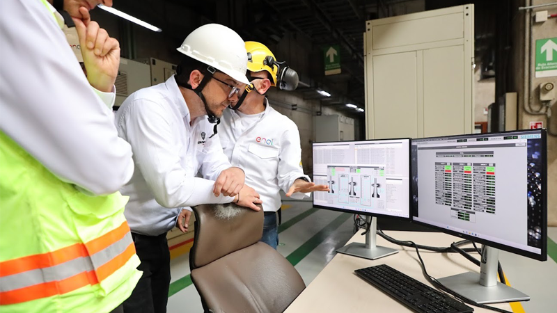 Tres hombres con cascos observan una pantalla de computadora, discutiendo información técnica.