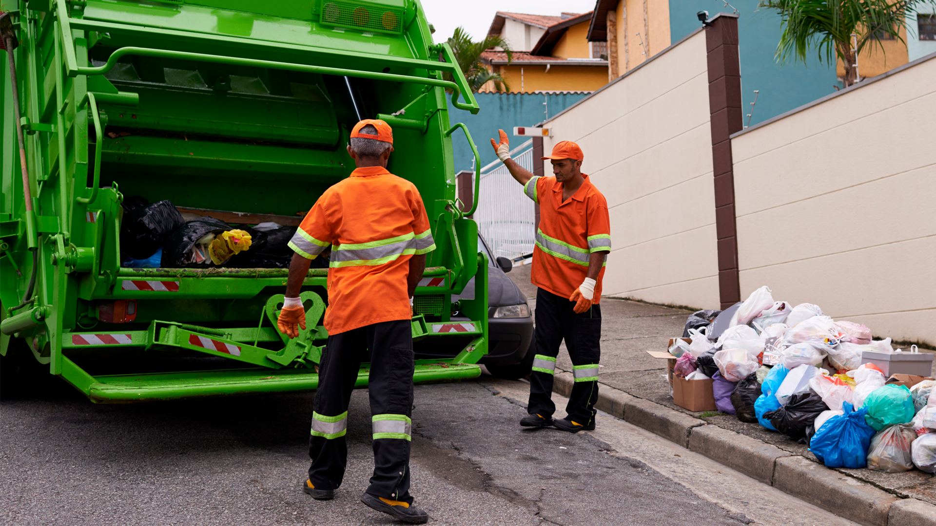 Operarios de una empresa de aseo urbano recolectan residuos domiciliarios con un camión compactador verde en una zona residencial