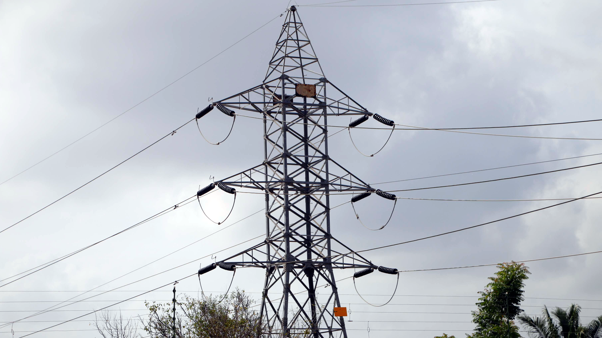 Torre de alta tensión con cables y un letrero visible